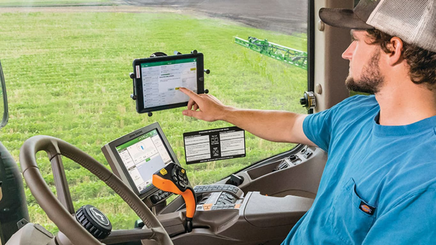 John Deere operator in the cab using the Operations Center on a mounted tablet and the in-dash display, out in the field