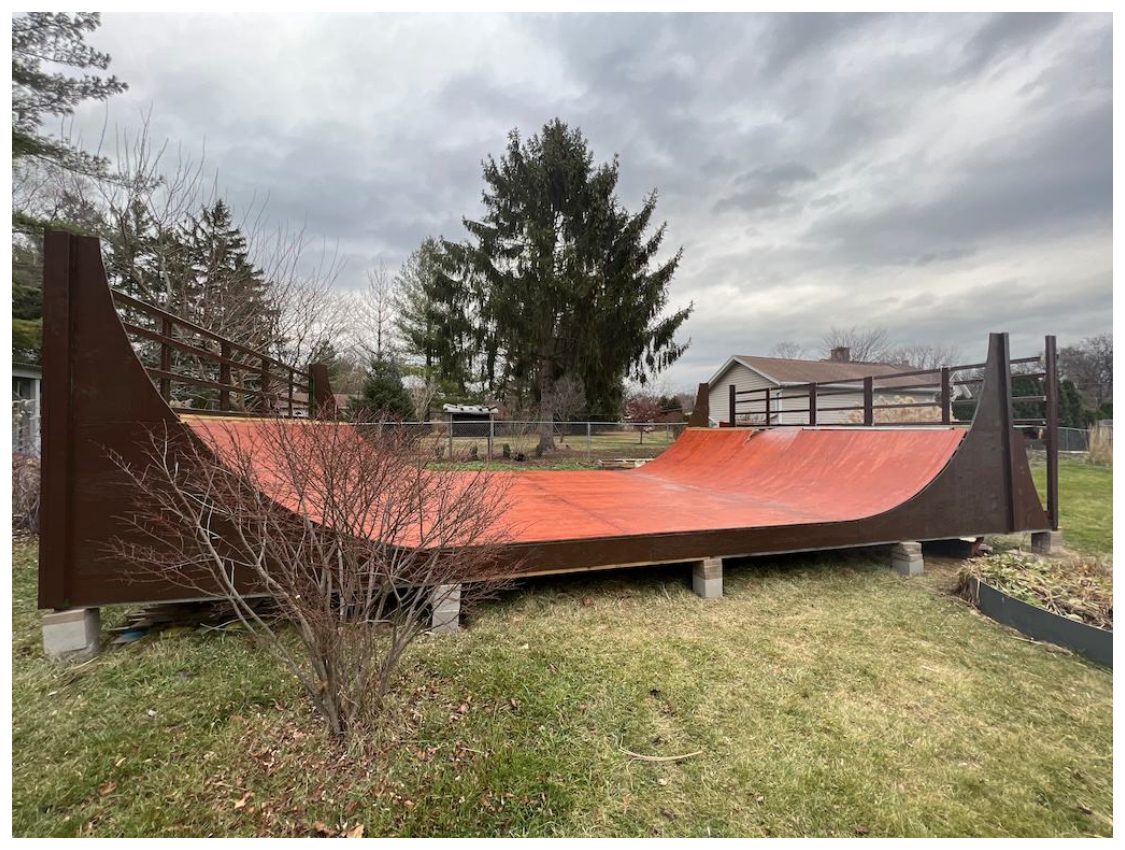 A large plywood half-pipe skate ramp built in a backyard, on a grey winter day.